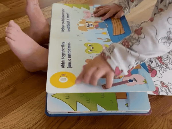 finger pressing the big button on the brushing buddies book cover
