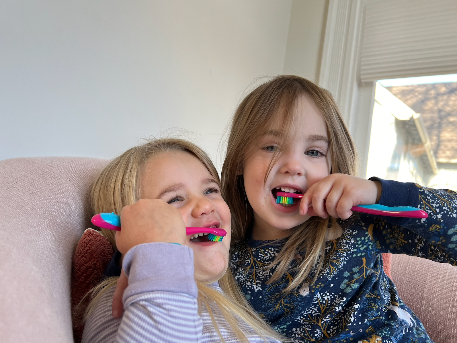two sisters mid-brushing with rainbow toothbrushes